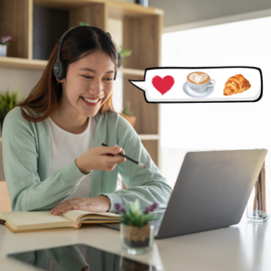Woman in a mint green sweater smiles during a video call, holding a pen. Speech bubble shows heart, coffee, and croissant. Light room.