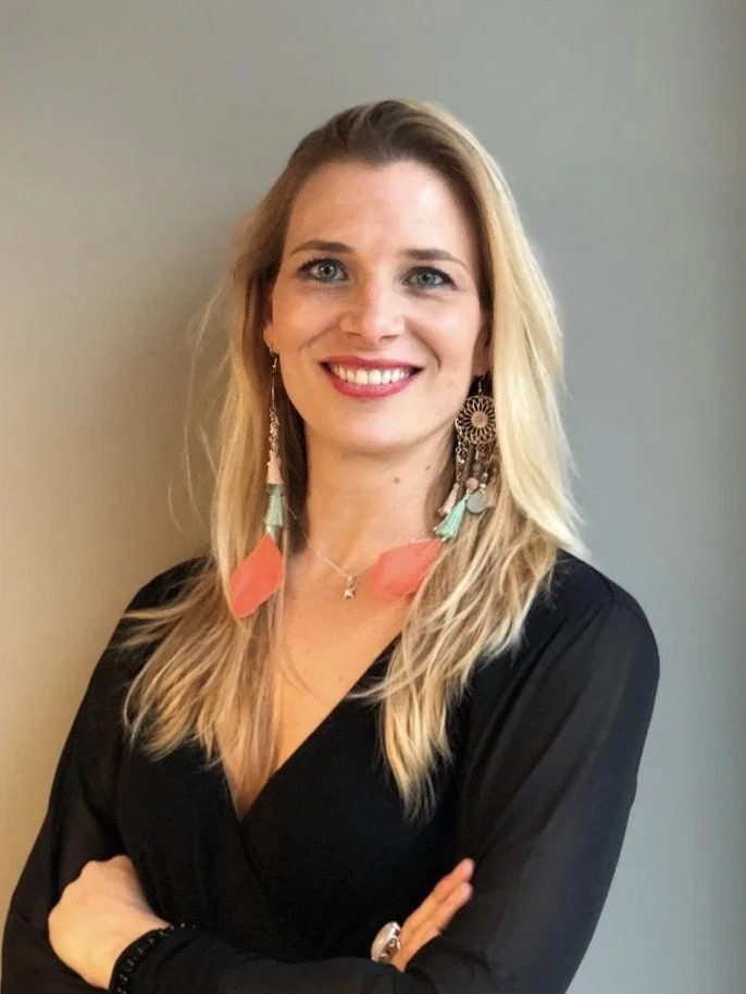 Belinda, French teacher at Sophie French Tutor, smiling with arms crossed wearing bold statement earrings