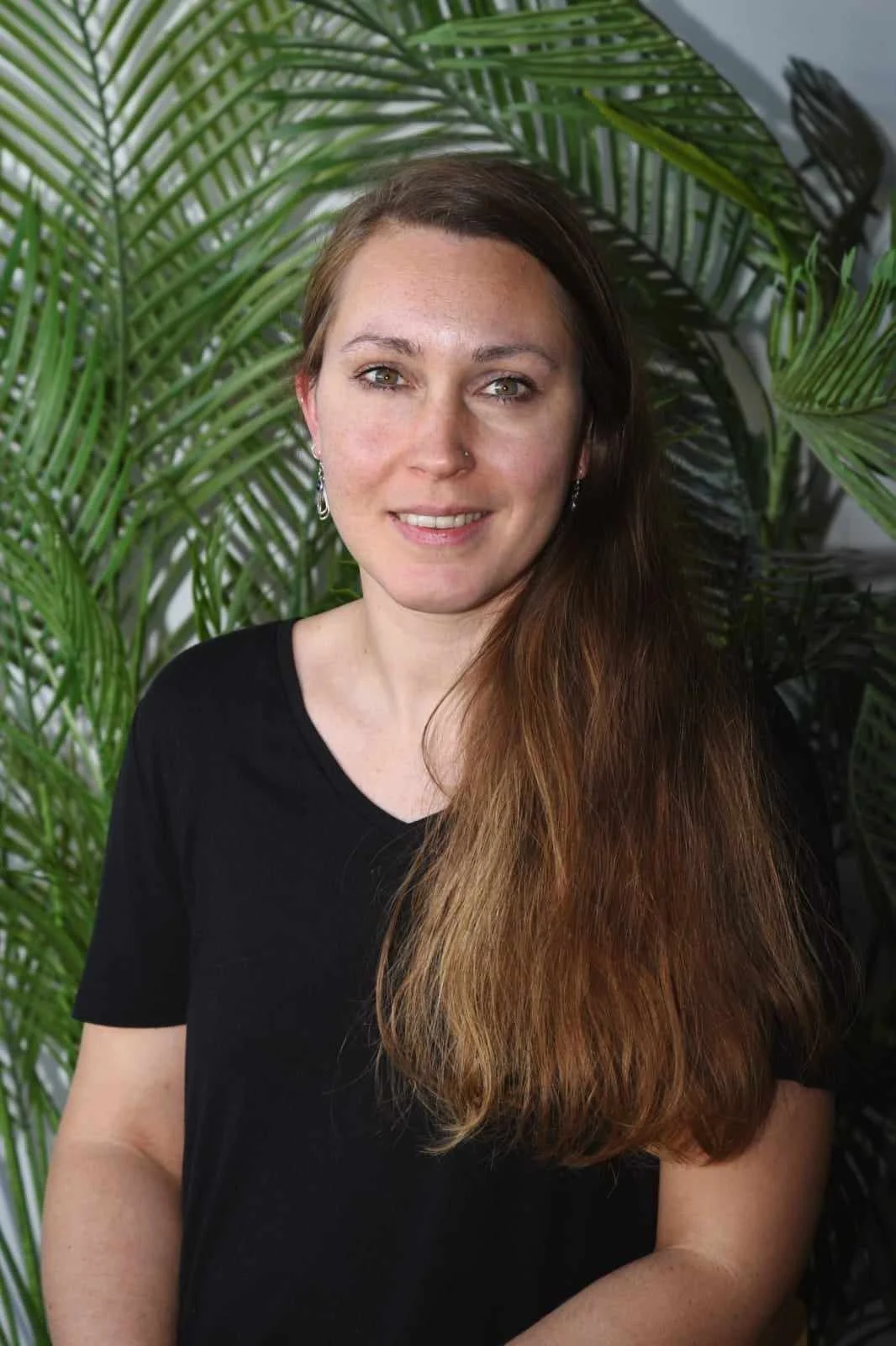 Astrid, French teacher at Sophie French Tutor, smiling with long hair in front of tropical green plant