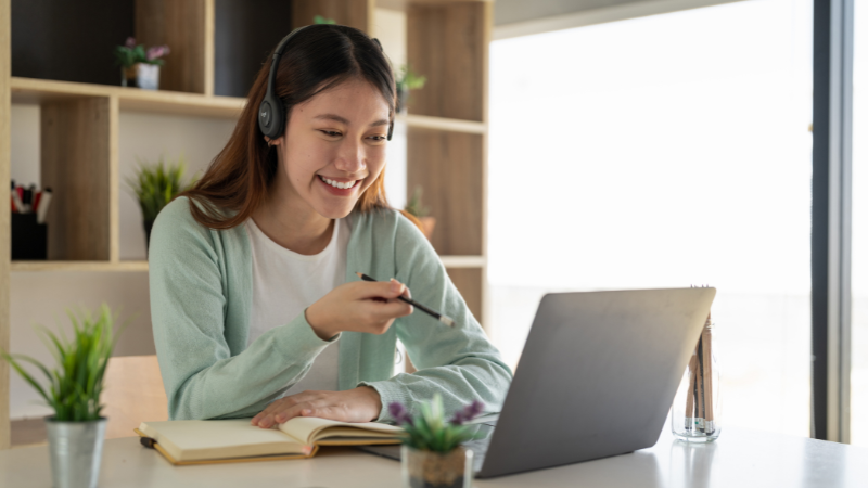 Woman smiling during an online French lesson, wearing headphones and taking notes in front of a laptop — private French lessons with a native tutor