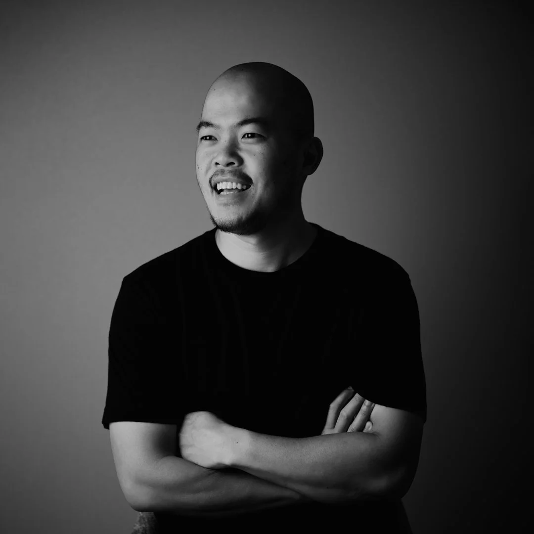 黒と白の背景の前に立つ若い男性が微笑んでいる。