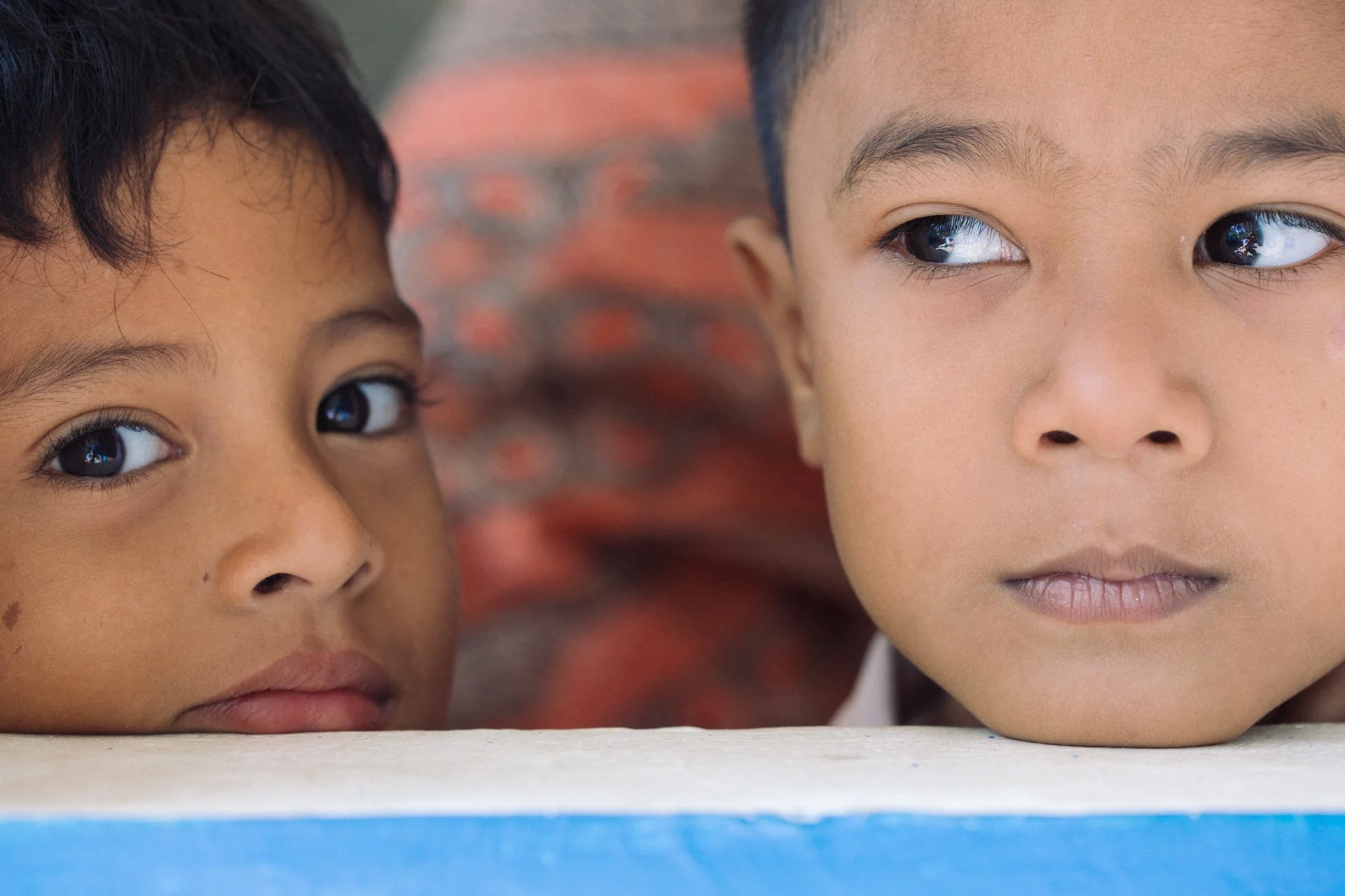 Close-up of two children's faces, one with darker skin and black hair on the left, and the other with lighter skin and short dark hair on the right, both looking forward with serious expressions.