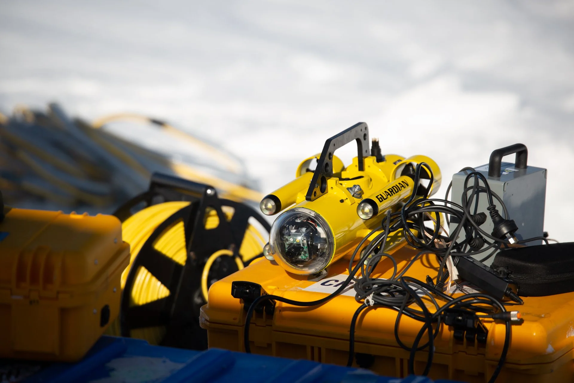 Close-up of yellow underwater robot with various wires and components, labeled 'Guardian', set against a cloudy sky.