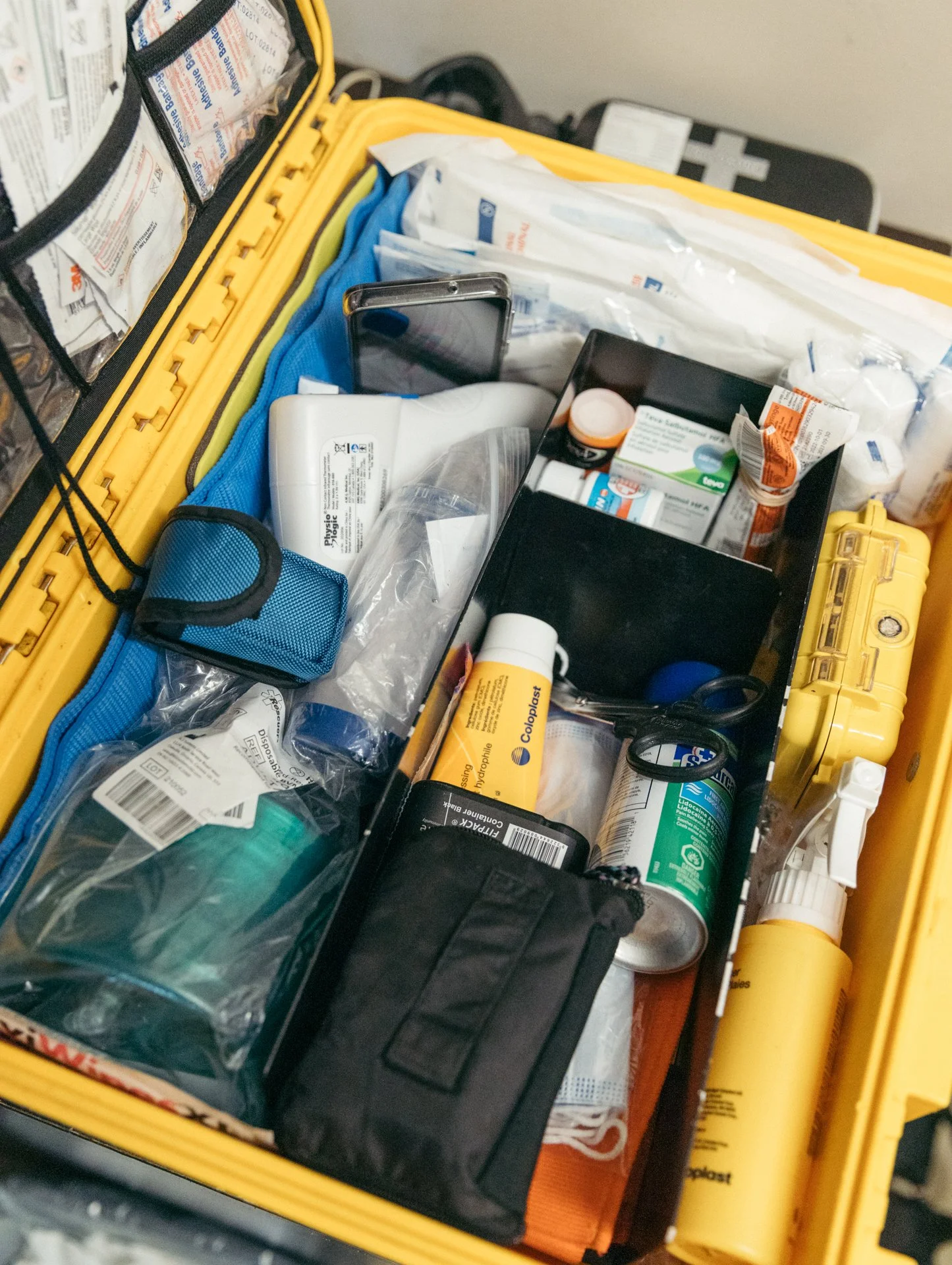 A medical emergency kit with various supplies, including medication bottles, bandages, and medical tools, organized inside a yellow plastic case.