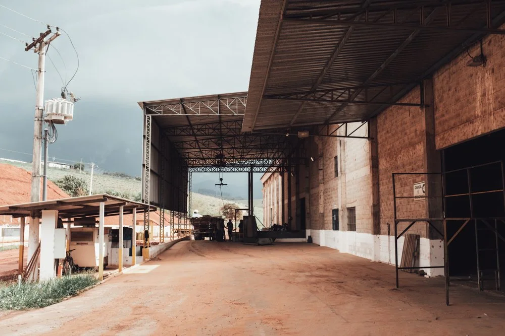 Industrial loading dock with trucks, a covered area, and a dirt road, with a cloudy sky overhead.