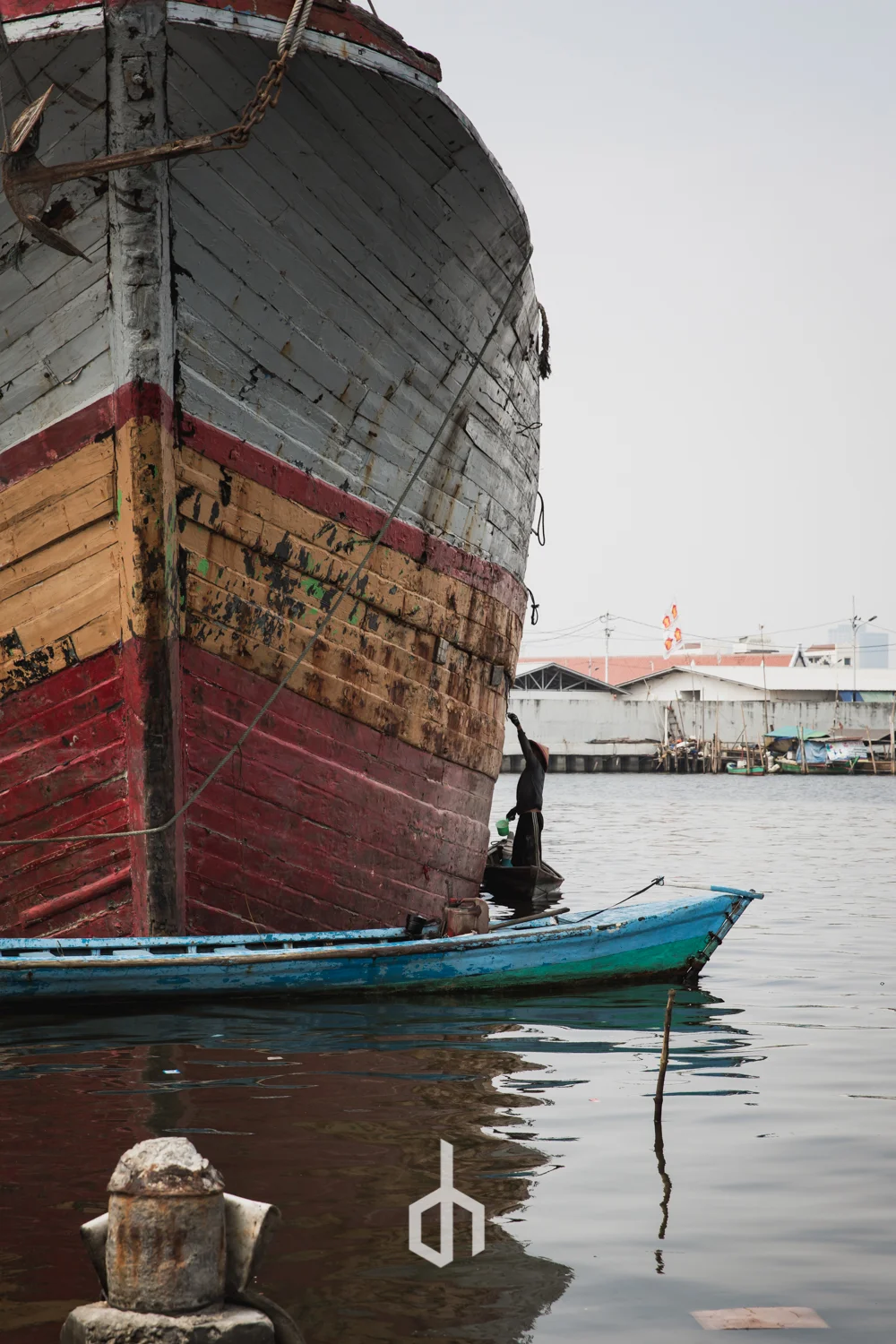 Close-up of a large, weathered boat docked at a harbor, with a smaller boat alongside and a person working on the large boat.