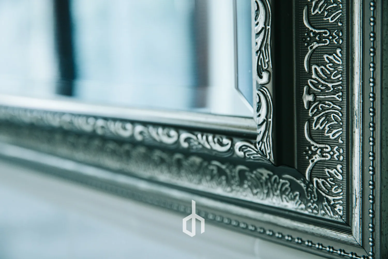 Close-up of a decorative silver mirror frame with ornate patterns, reflecting a blurred background.