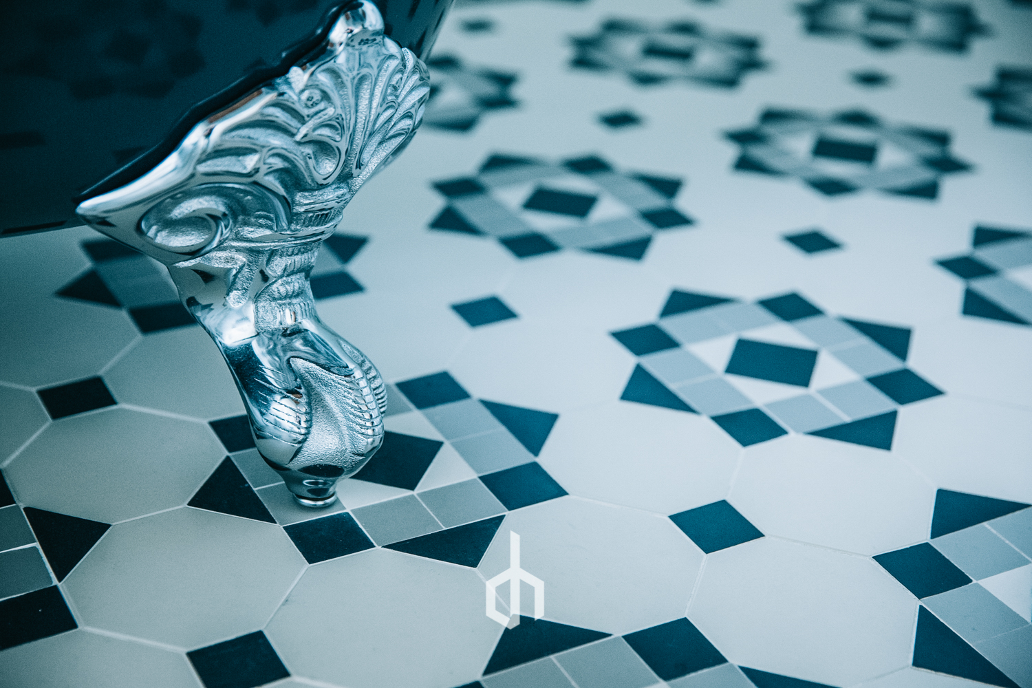 Close-up of a silver, ornate faucet handle on a tiled floor with geometric patterns in black, white, gray, and blue.