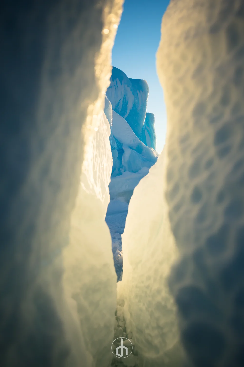 Iceberg crevasse revealing a distant glacier under a clear blue sky.
