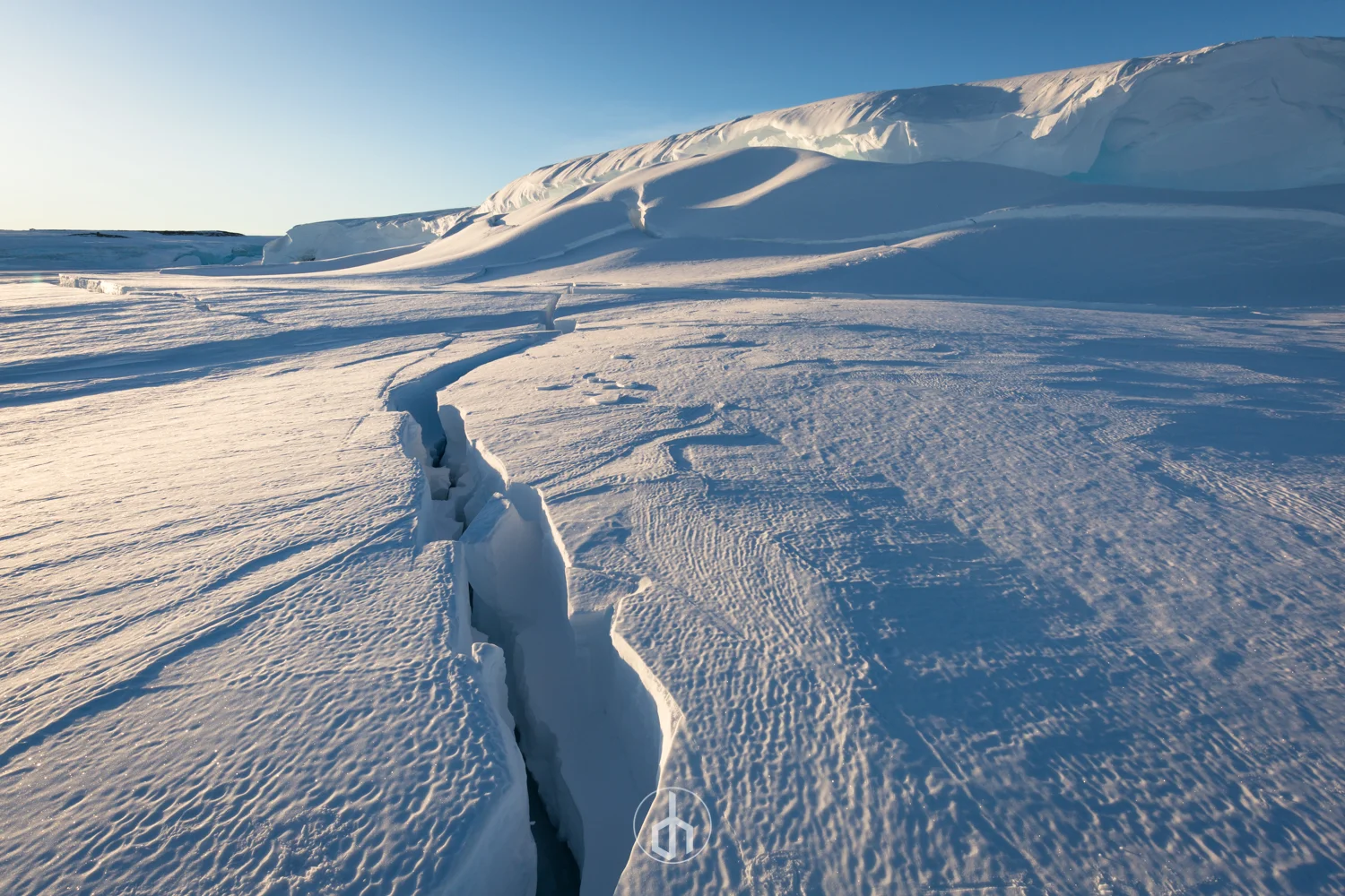 Snow-covered landscape with a large crack in the ice and a clear blue sky.