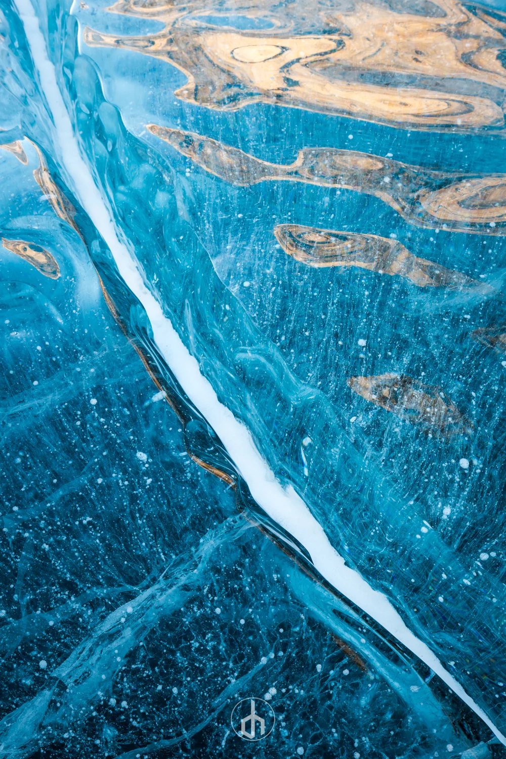 Close-up of blue ice with visible cracks and bubbles, reflecting light, with a small white logo at the bottom center.