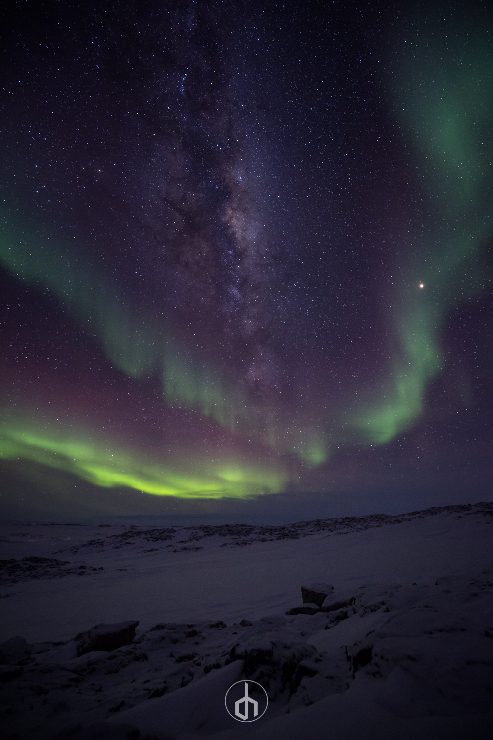 Night sky with the Milky Way galaxy and green northern lights over snow-covered landscape.
