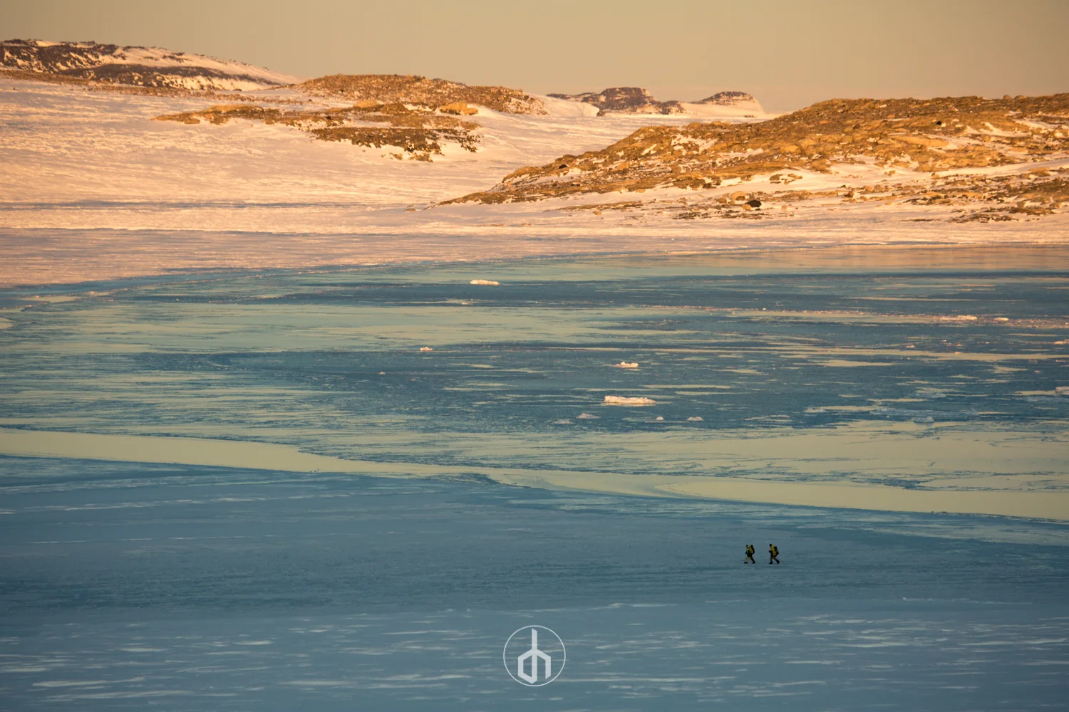 A snow-covered, icy landscape with two explorers hiking across the frozen terrain, with a logo at the bottom center.