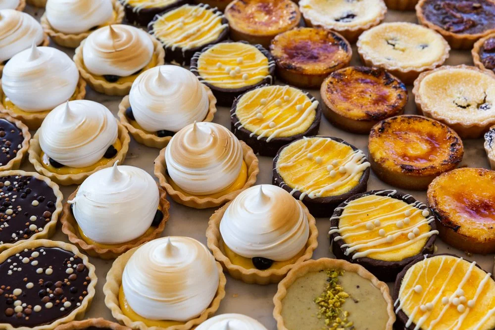 An assortment of assorted mini tarts including lemon meringue, chocolate topped, and custard tarts.