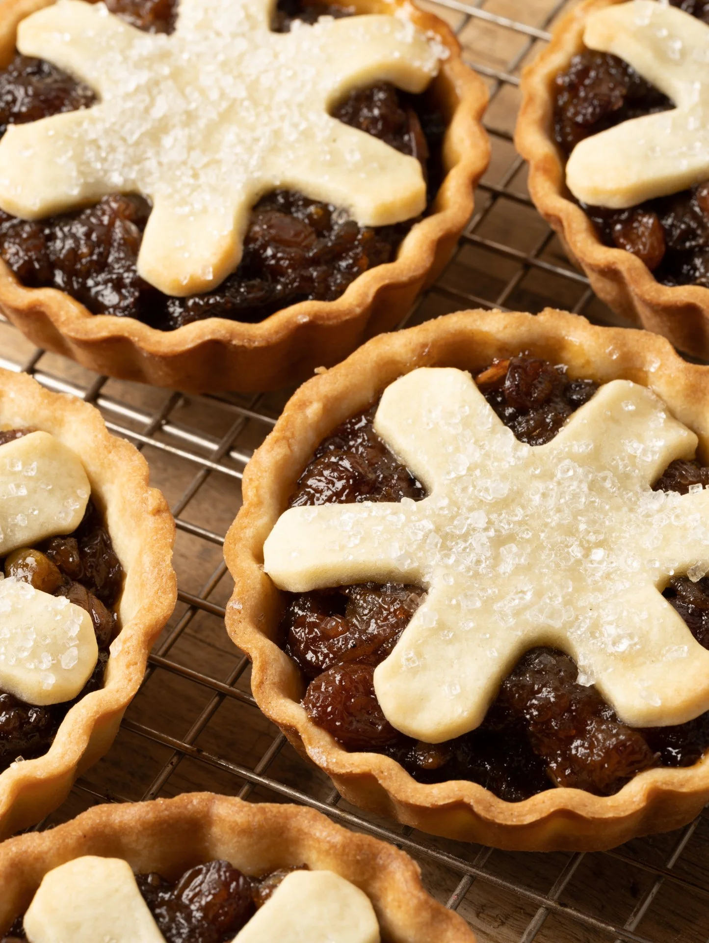 Close-up of freshly baked mini tartlets with a golden crust, filled with dark fruit jam, topped with a white chocolate or sugar decoration in the shape of a star.