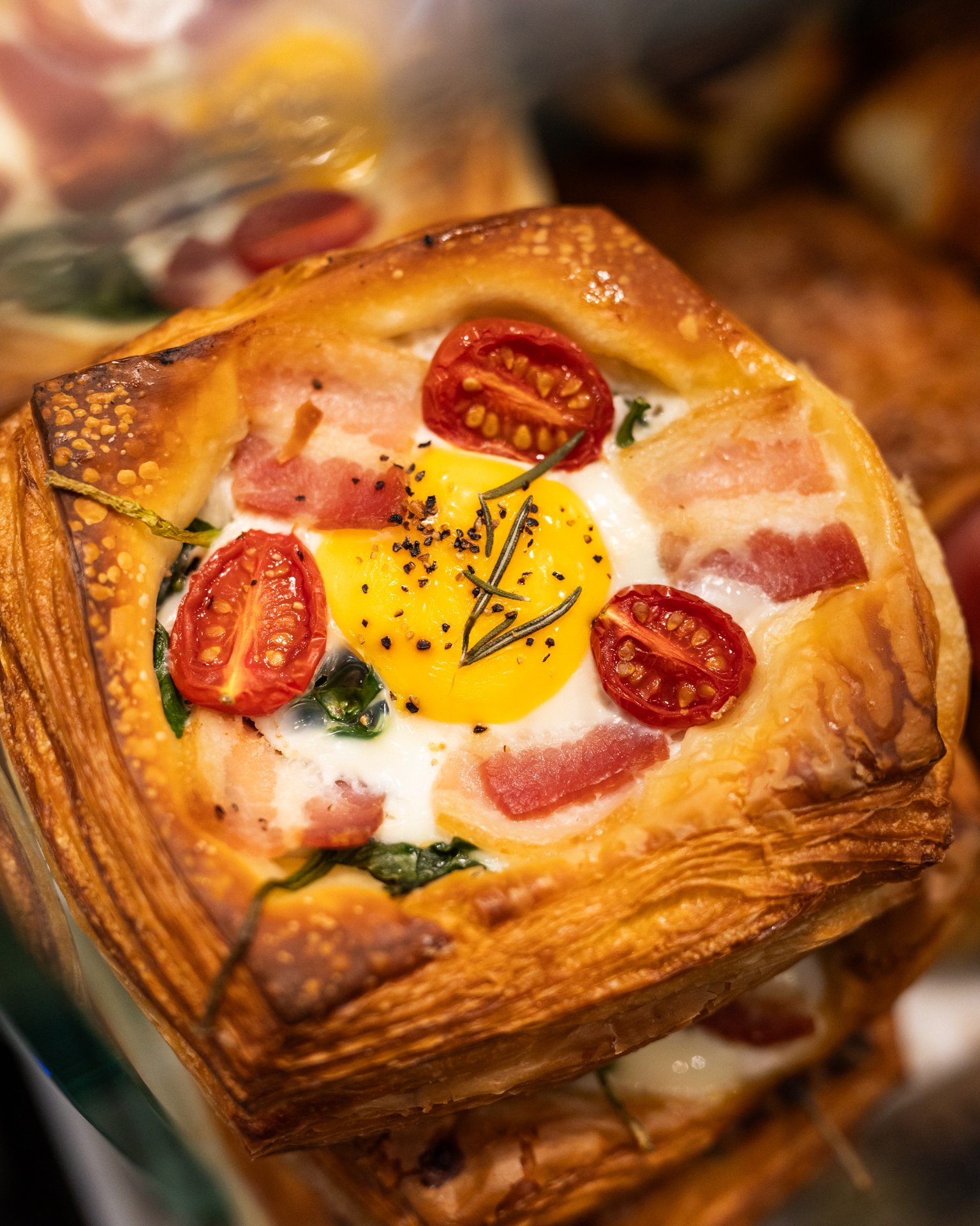 Baked pastry with a golden crust, topped with cherry tomatoes, a sunny side up egg, black pepper, and herbs inside a savory pie crust.