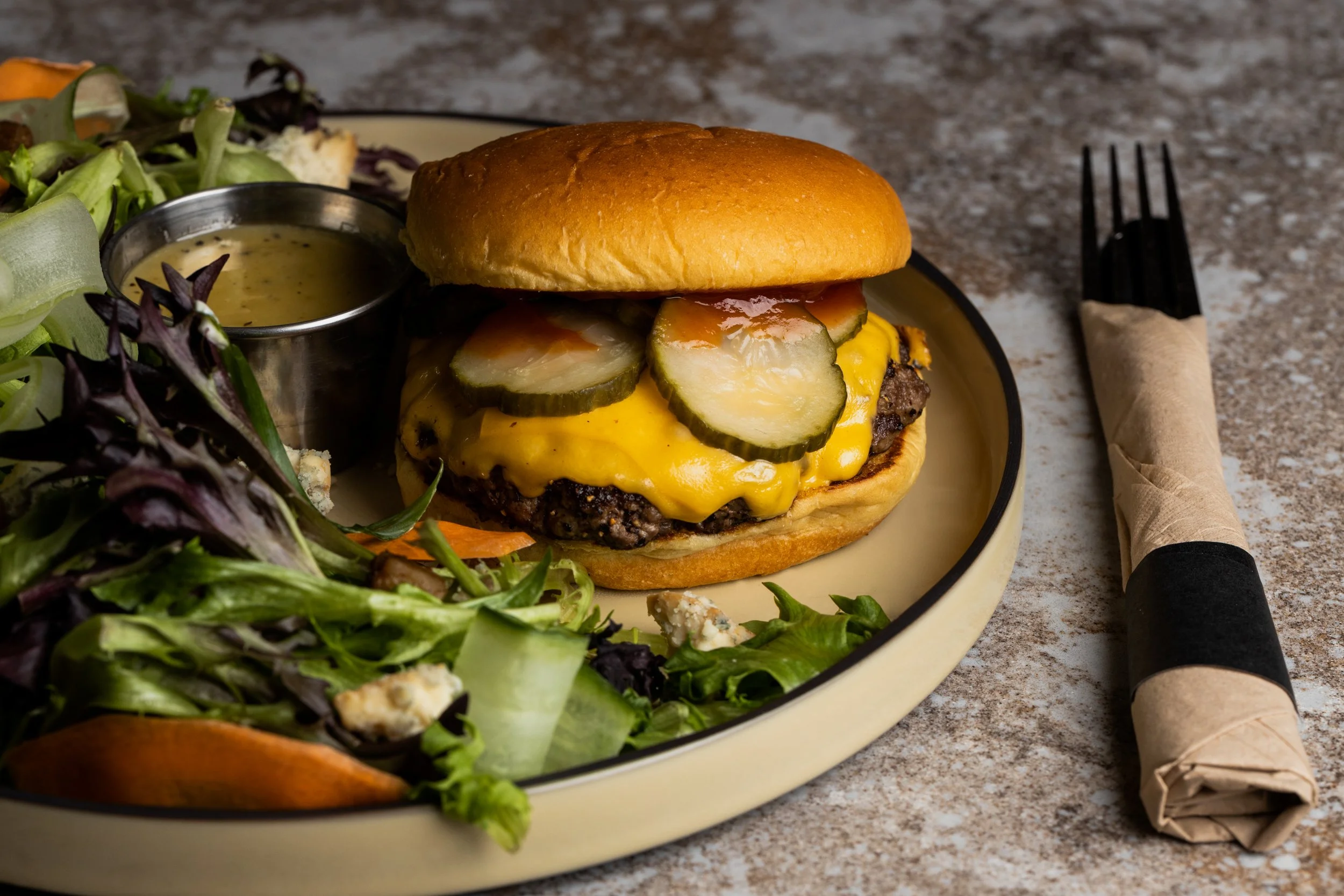 Cheeseburger with pickles, lettuce, and mustard, served with a side salad