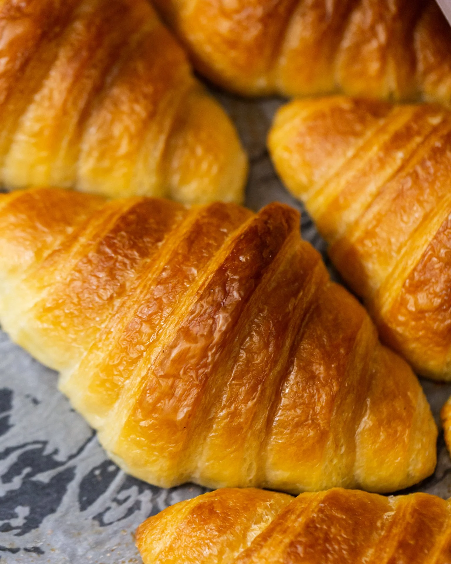 Close-up of freshly baked croissants with golden-brown, flaky crusts, arranged on a textured surface.