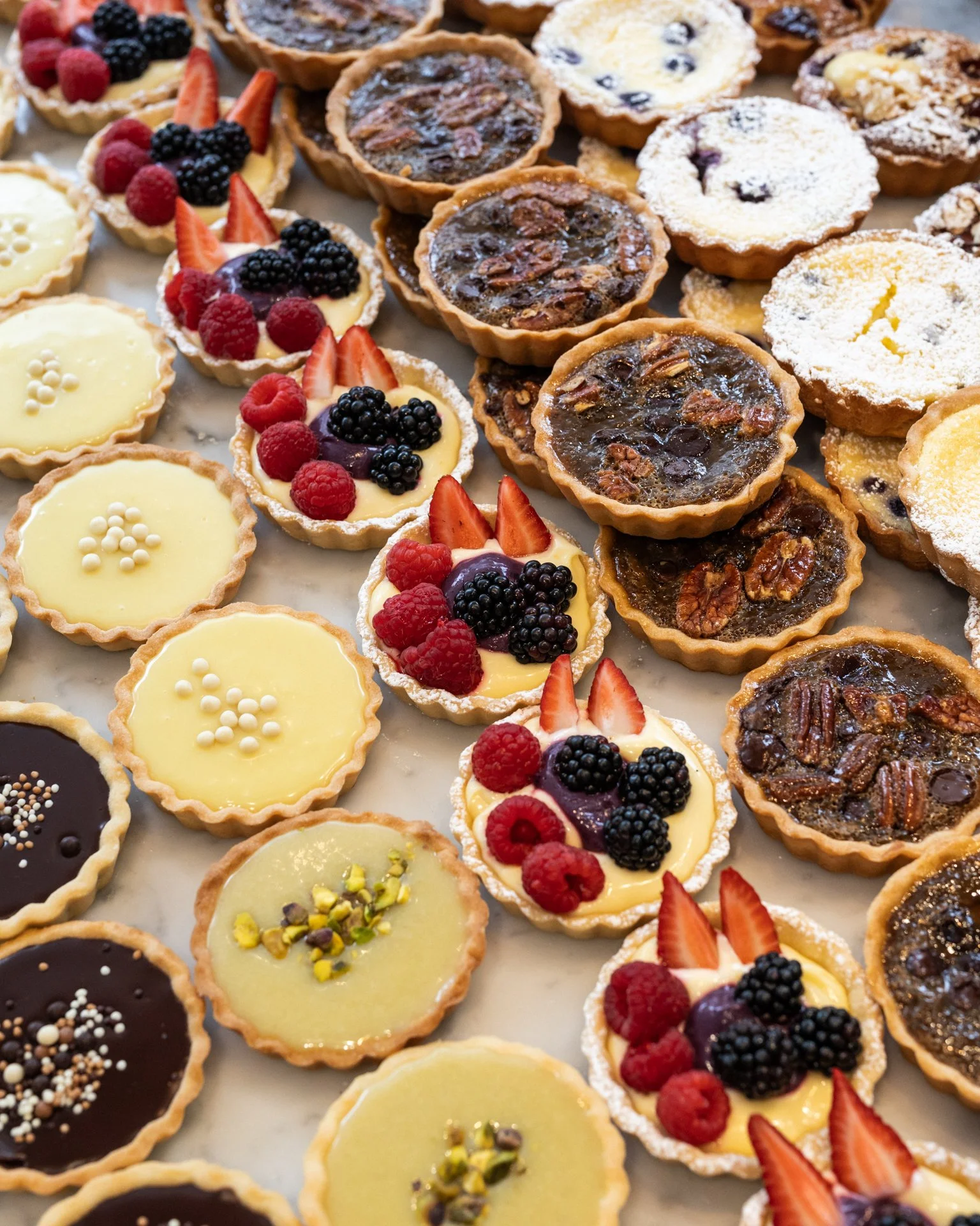 Assorted fruit tarts with various toppings including berries, sliced strawberries, and nuts arranged on a white surface.
