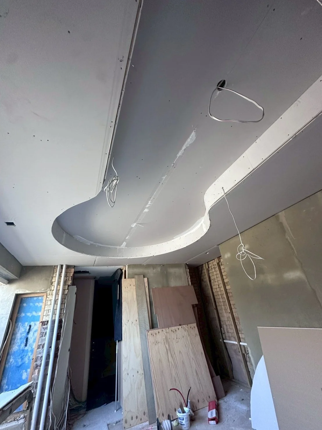 Construction site with a ceiling being installed, wires hanging from the ceiling, and unfinished walls and floor.