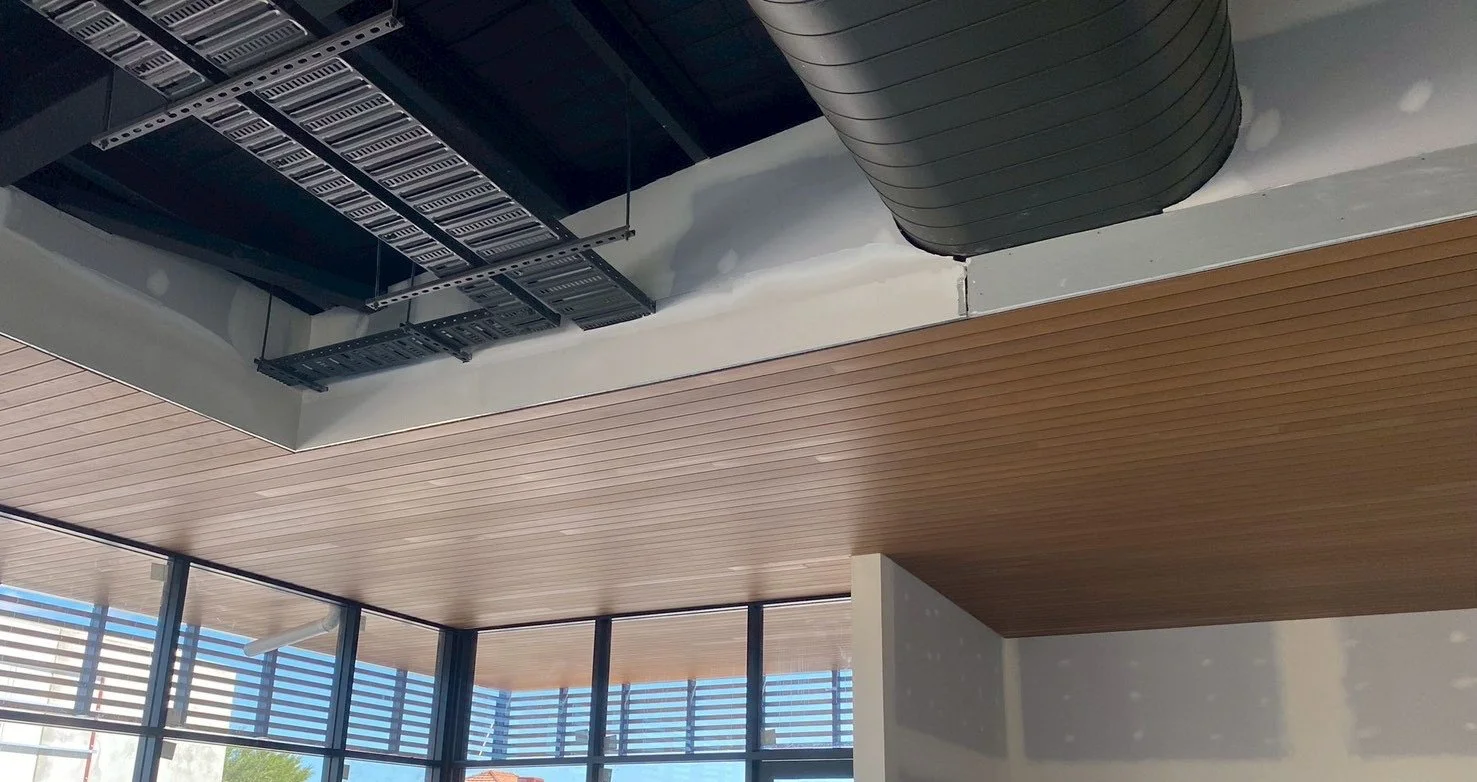 View of an indoor ceiling with wooden paneling, large windows, ceiling ducts, and cable trays.