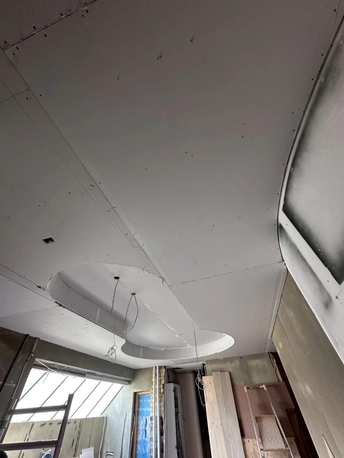 Construction site with a partially finished ceiling, drywall panels, and wires hanging from the ceiling.