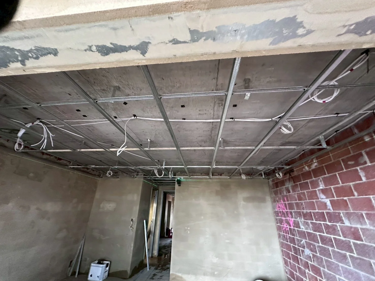 Under construction room with exposed ceiling framing, electrical wiring, and unfinished brick and drywall walls.