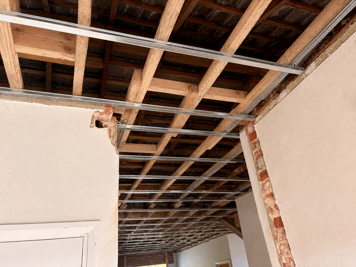 Partially demolished interior wall with exposed brick and drywall, showing metal framing and wooden ceiling joists.