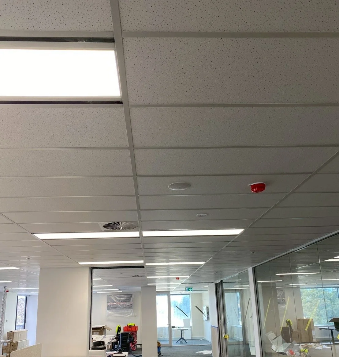 Ceiling in an office space with fluorescent lights, smoke detector, and a red fire alarm.