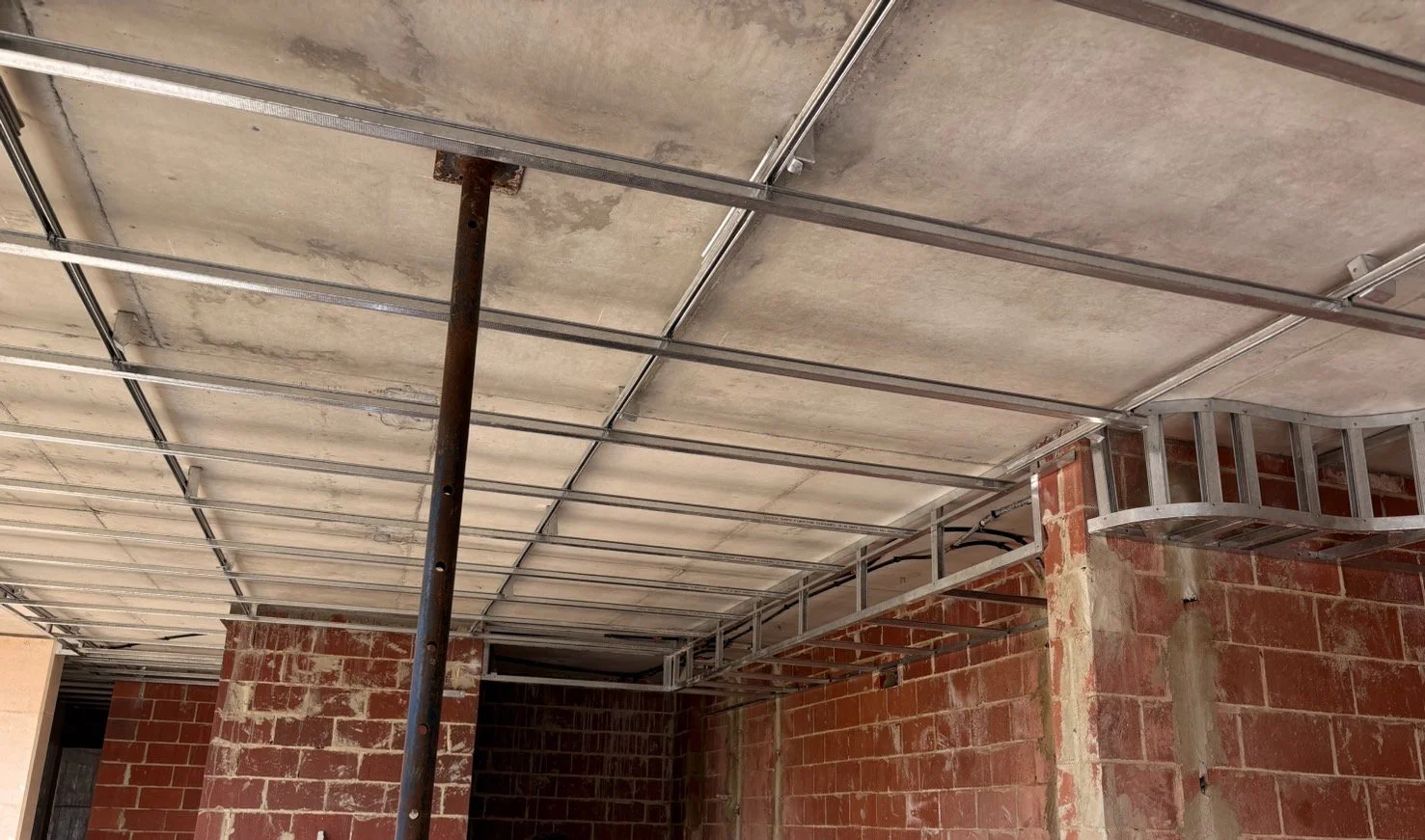 Construction site with exposed brick walls and metal framing for a ceiling or roof.