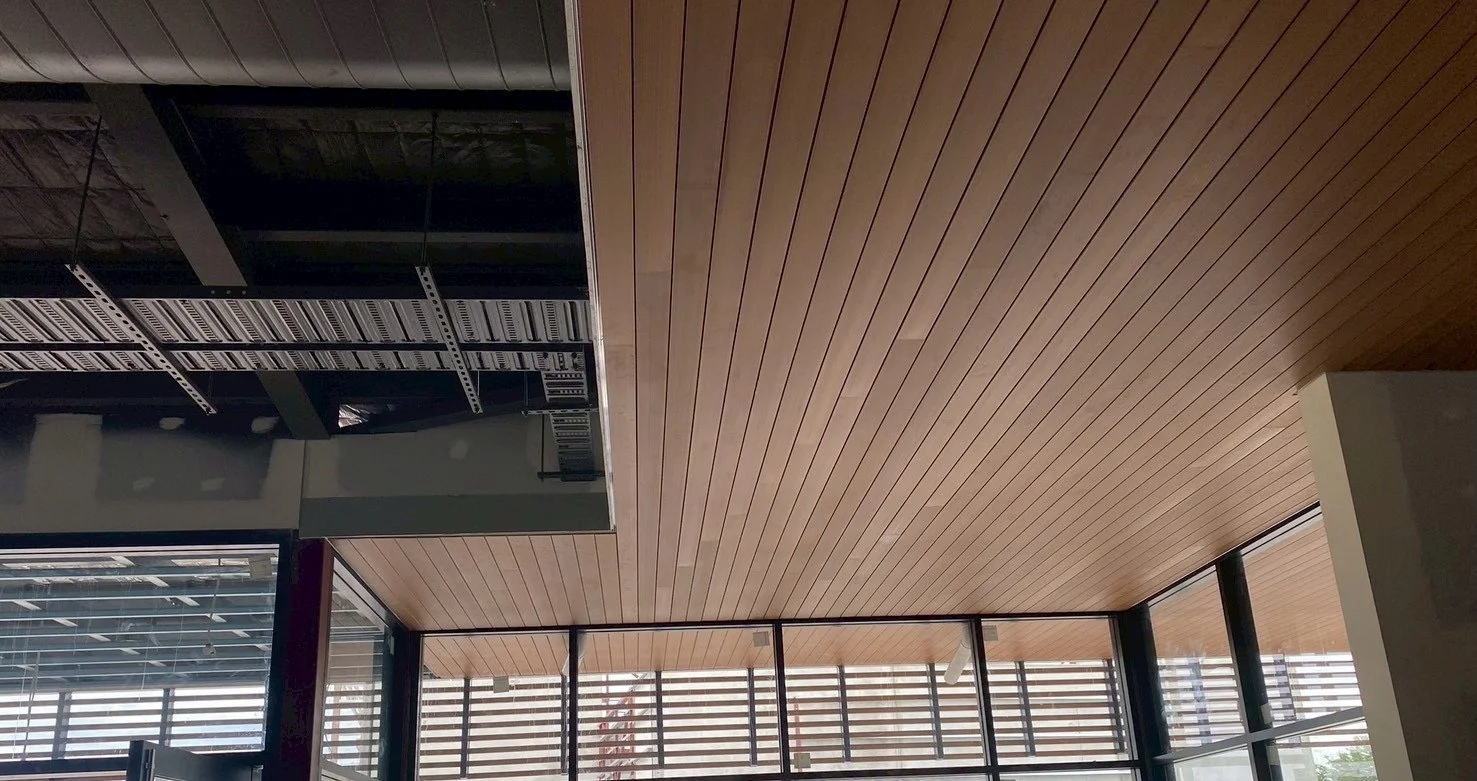 Interior of a modern building with a wooden ceiling, large glass windows, and an exposed area with structural elements or shelving.