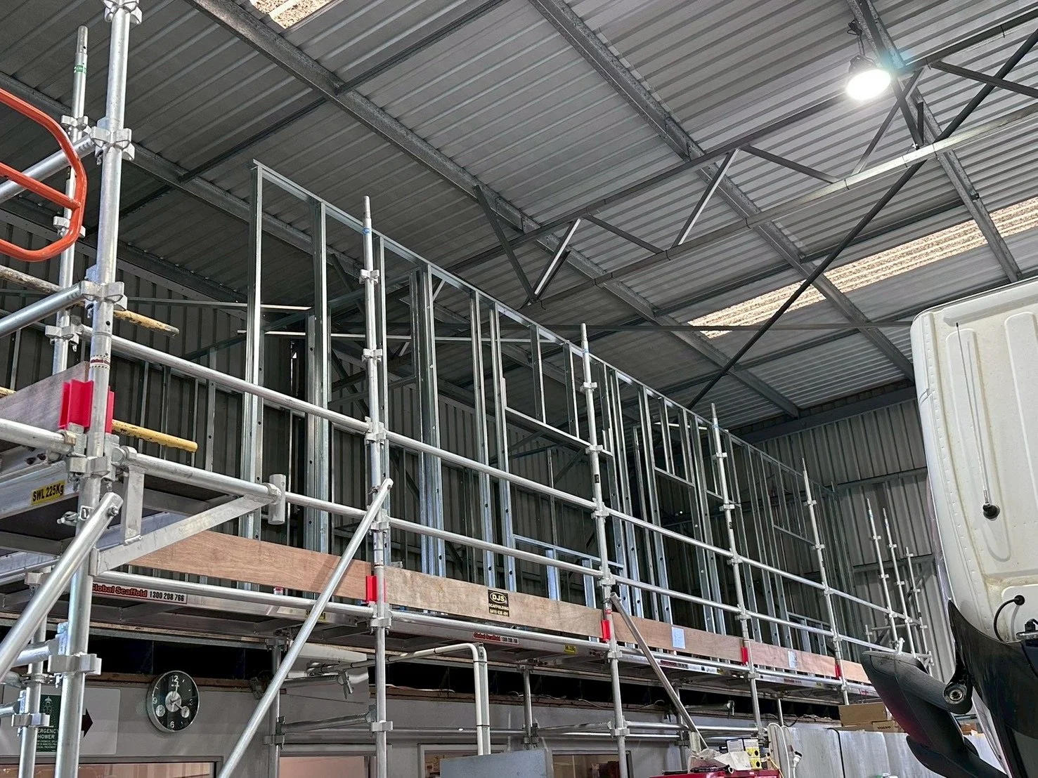 Interior of a building under construction with metal framework scaffolding, a corrugated metal roof, and some construction equipment.