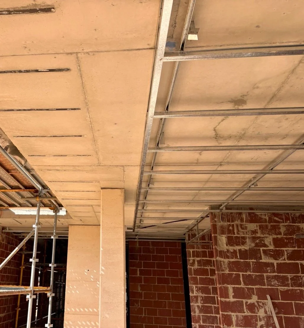 Construction site interior with exposed brick walls, unfinished ceiling with metal framing, and scaffolding on the left side.