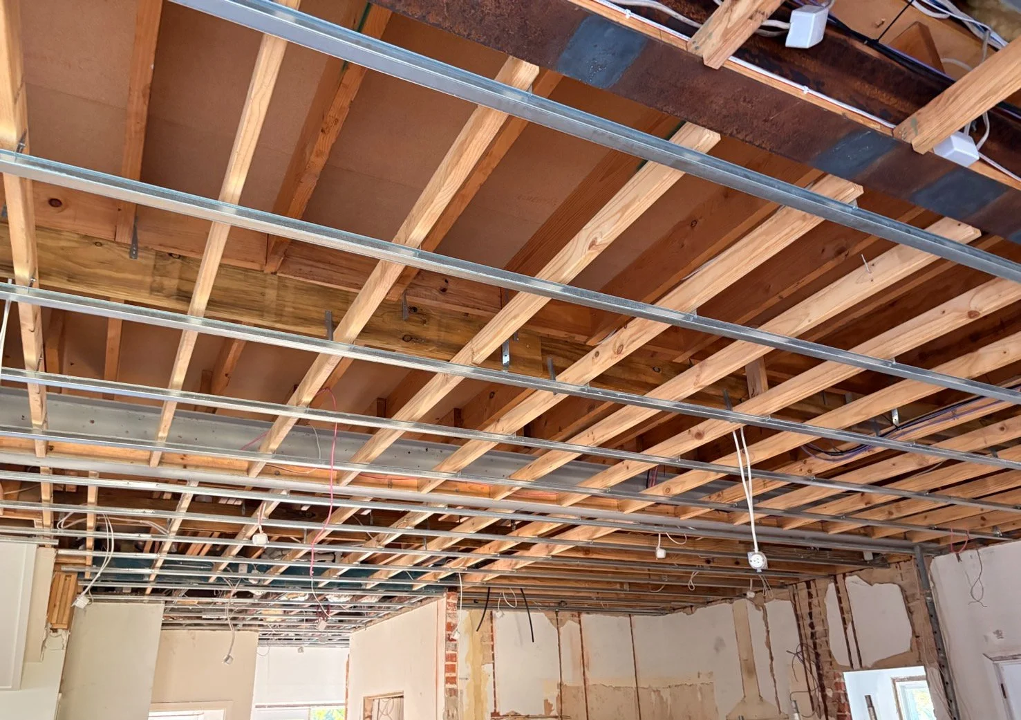 Interior of a building under construction showing exposed wooden ceiling rafters, metal support beams, and electrical wiring in the ceiling.