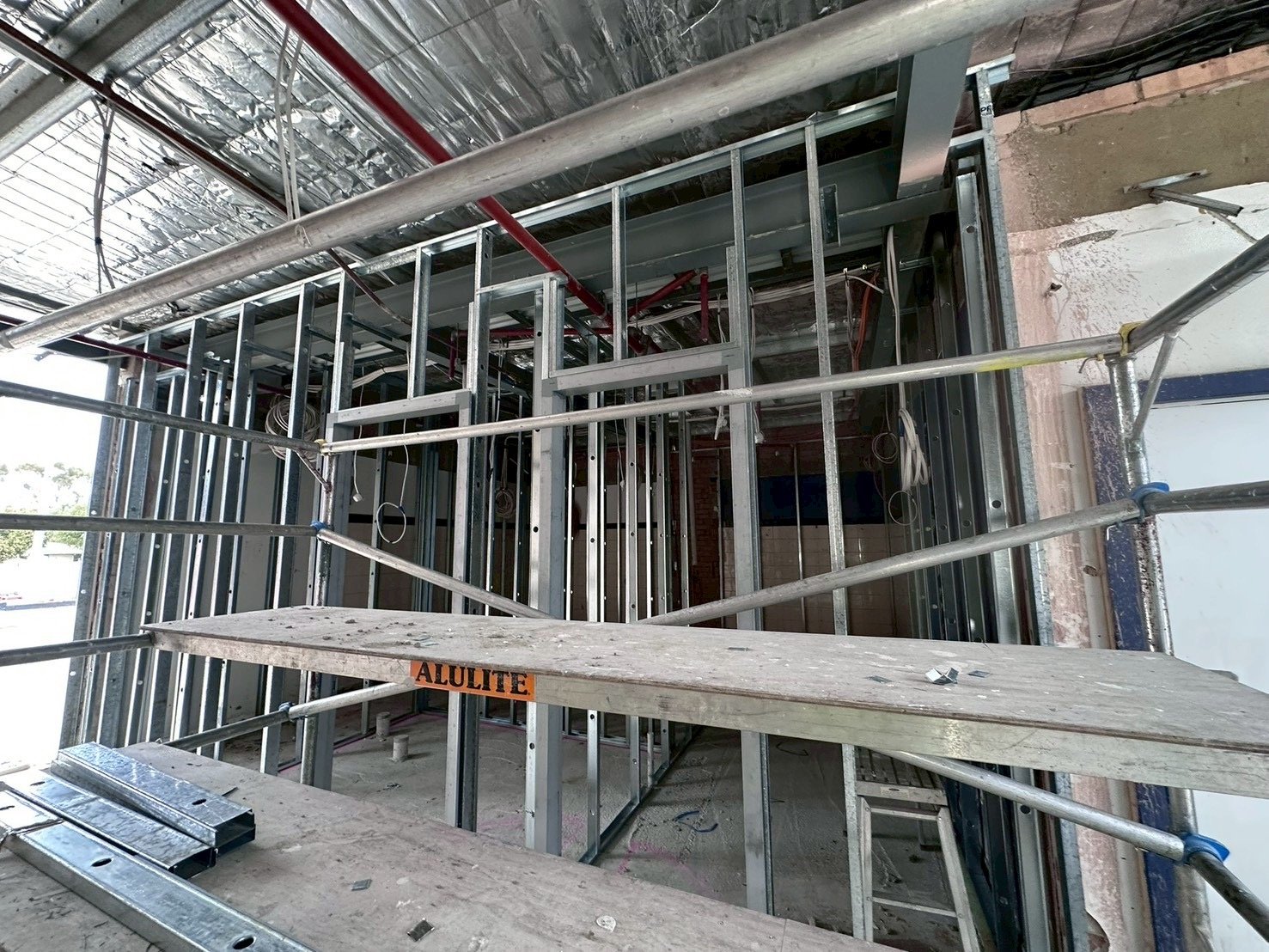 Construction site with metal framing, scaffolding, and electrical wiring in progress.