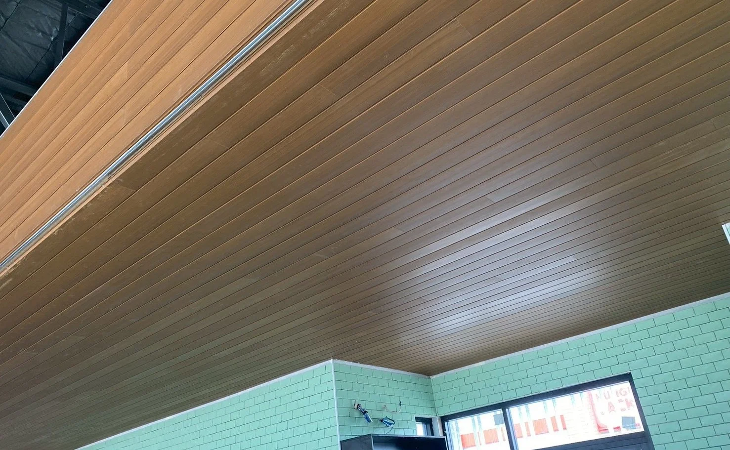 Ceiling with wooden slats, corner of a room with green brick walls, and windows showing an exterior sign that says "LUNG".