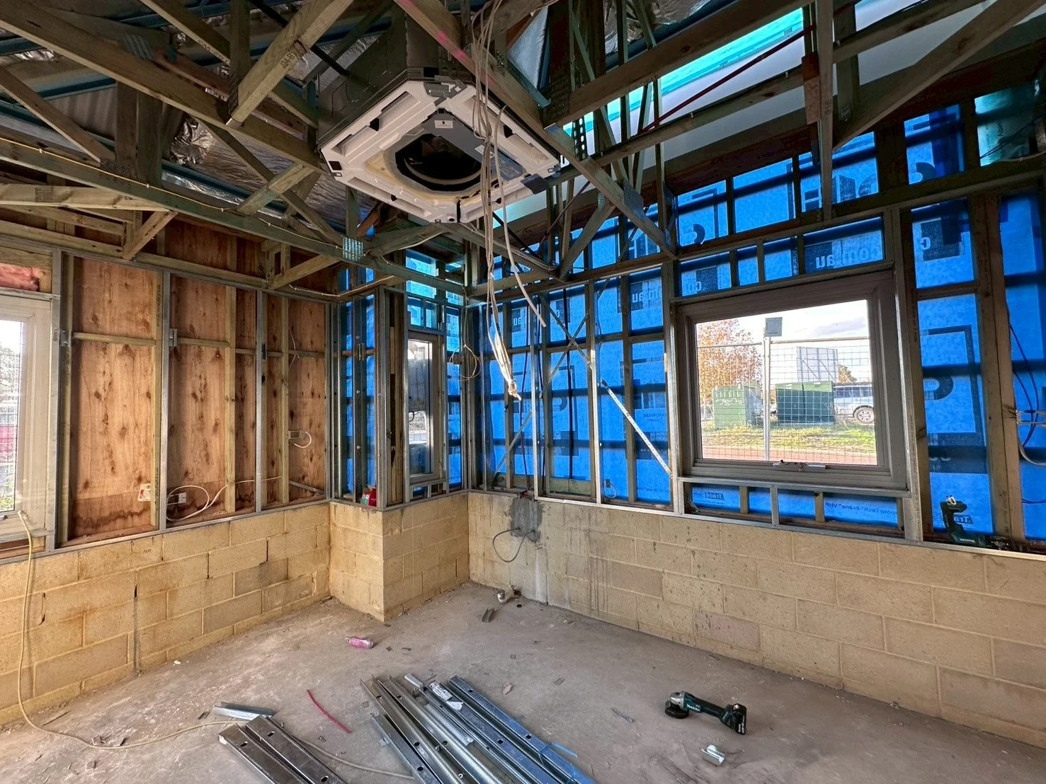 Interior of a house under construction with exposed wooden framing, insulation, and a window, showing construction tools and materials on the floor.