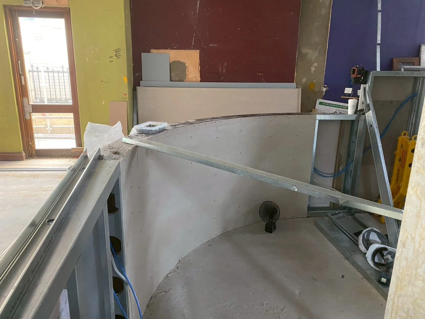 Interior of a construction site with metal framework and an arched table or counter being assembled, with tools and construction materials scattered around.