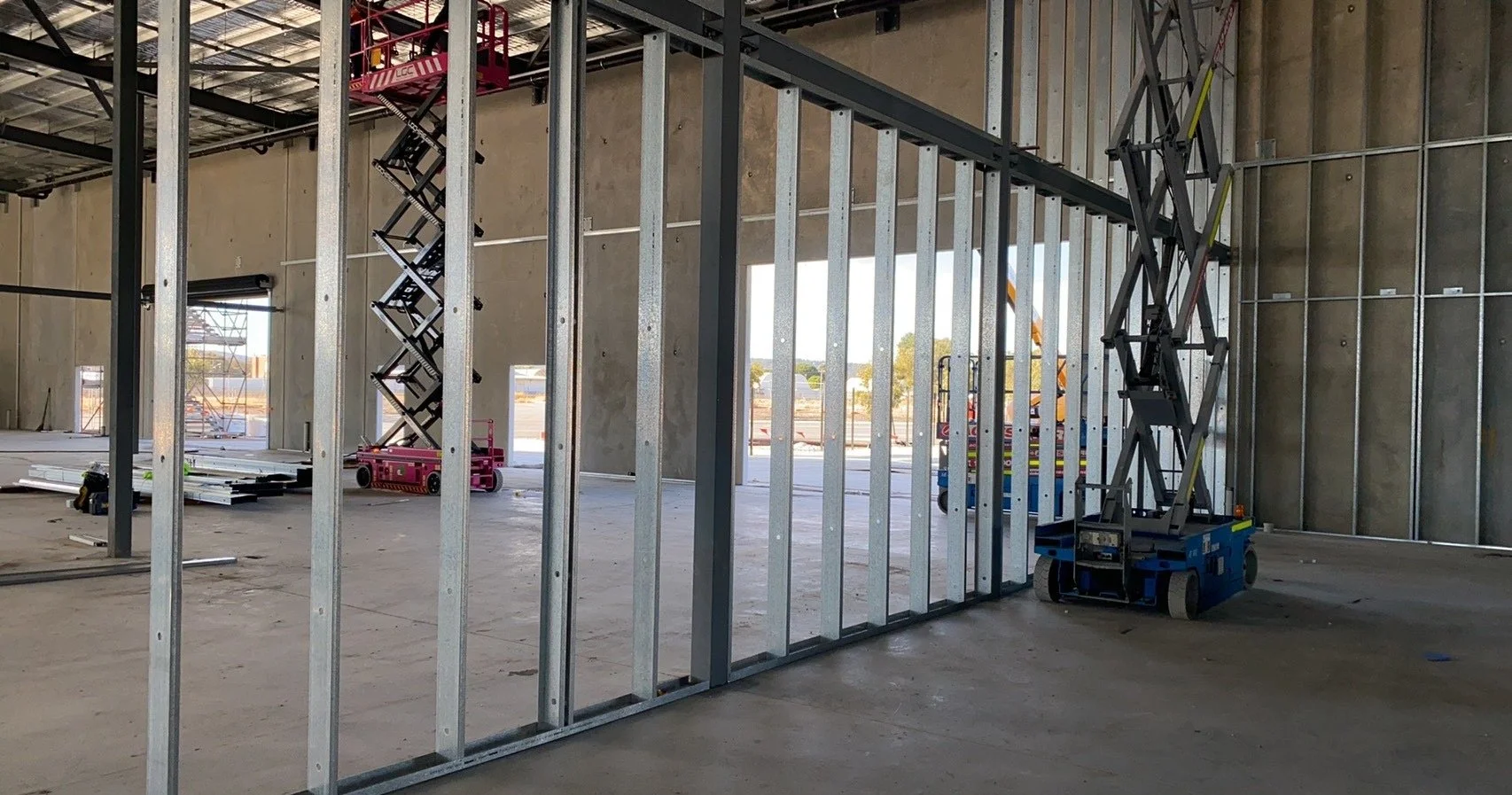 Construction site with metal framing, scissor lifts, and tools inside a building under construction.