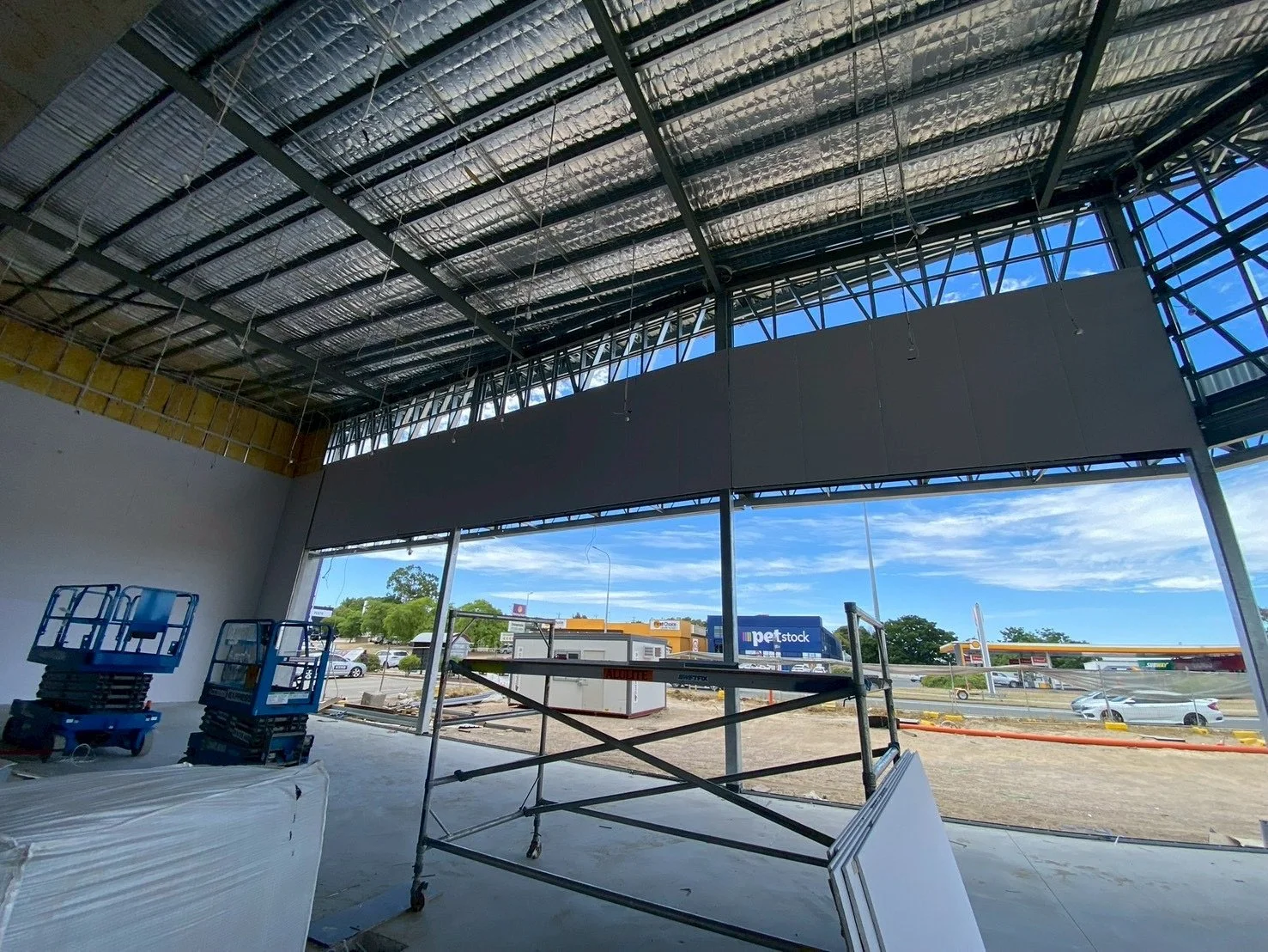 Interior of a commercial building under construction, showing large windows, construction scaffolding, and building materials in the space.