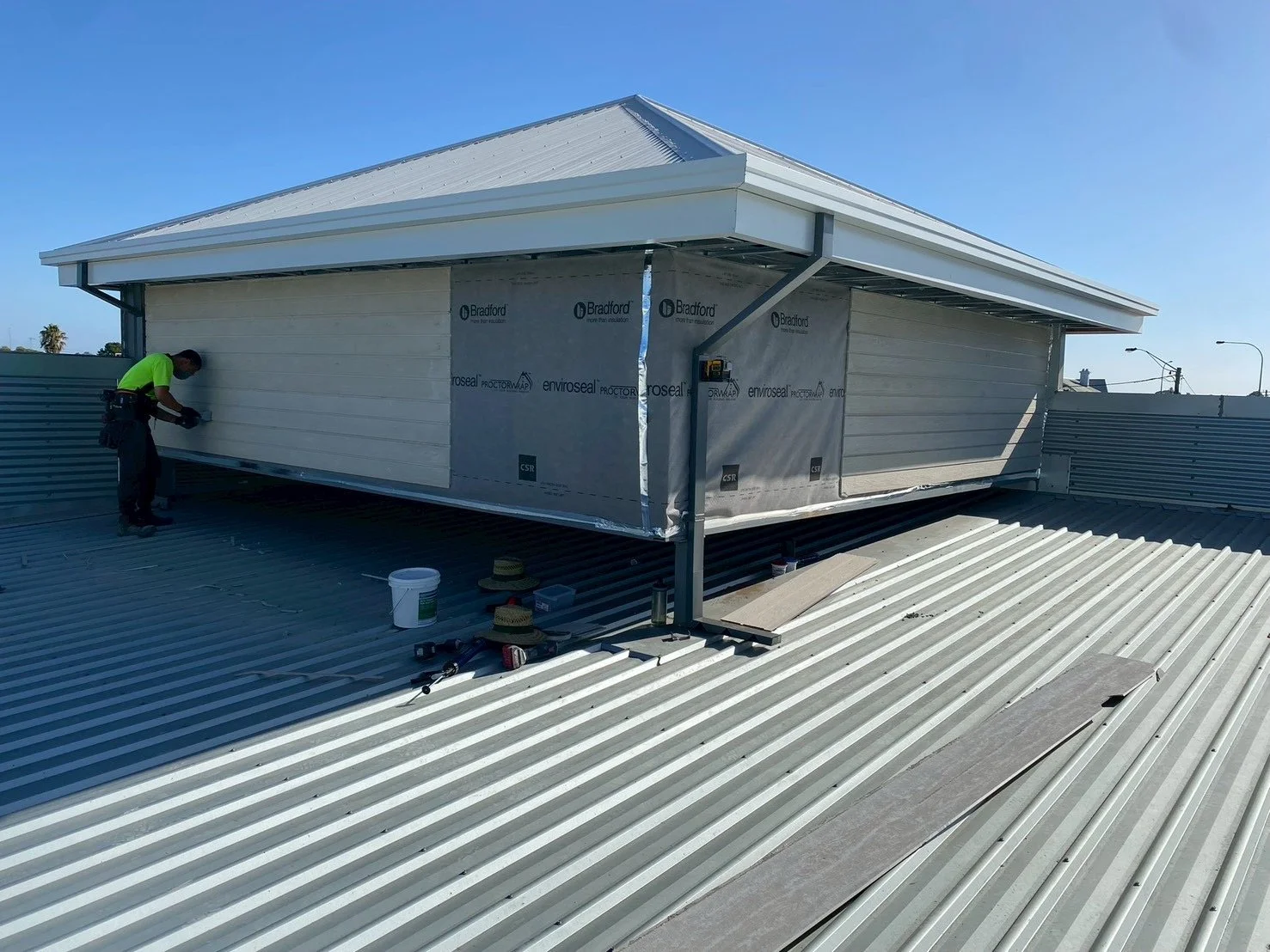 Construction worker installing exterior siding on a rooftop structure with metal siding and roofing.