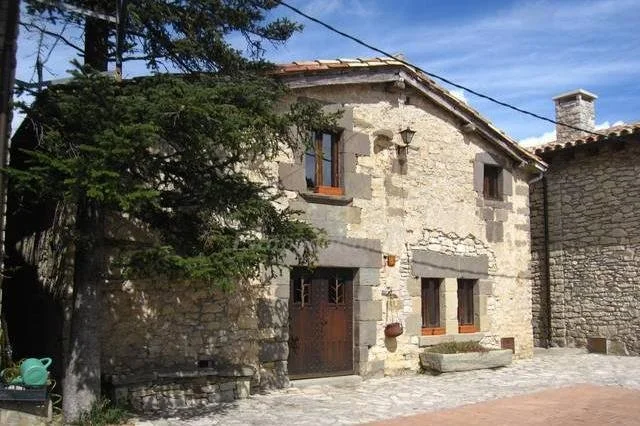 Casa de piedra con ventanas de madera y árbol en el frente en un día soleado