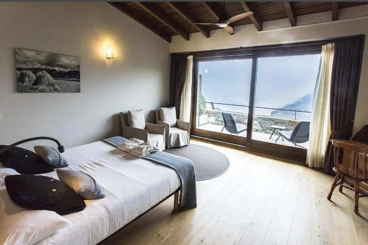 Habitación con cama, sofá, vista a la montaña y balcón con sillas.