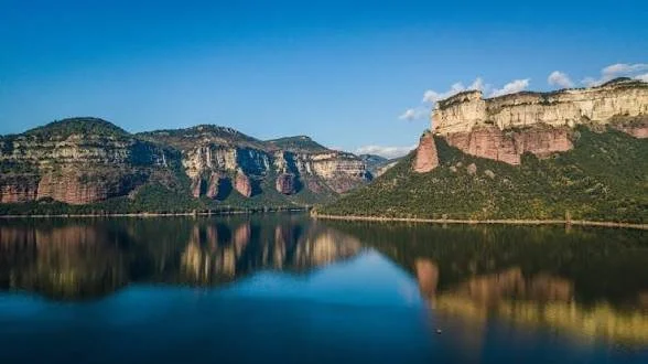 Paisaje de montañas y un lago reflejando el cielo azul.