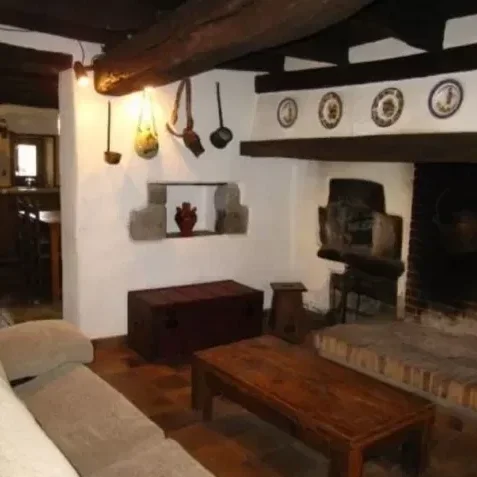 Interior de una sala con muebles de madera, una chimenea de piedra y decoración rústica en la pared, incluyendo platos y cucharas de madera colgadas.