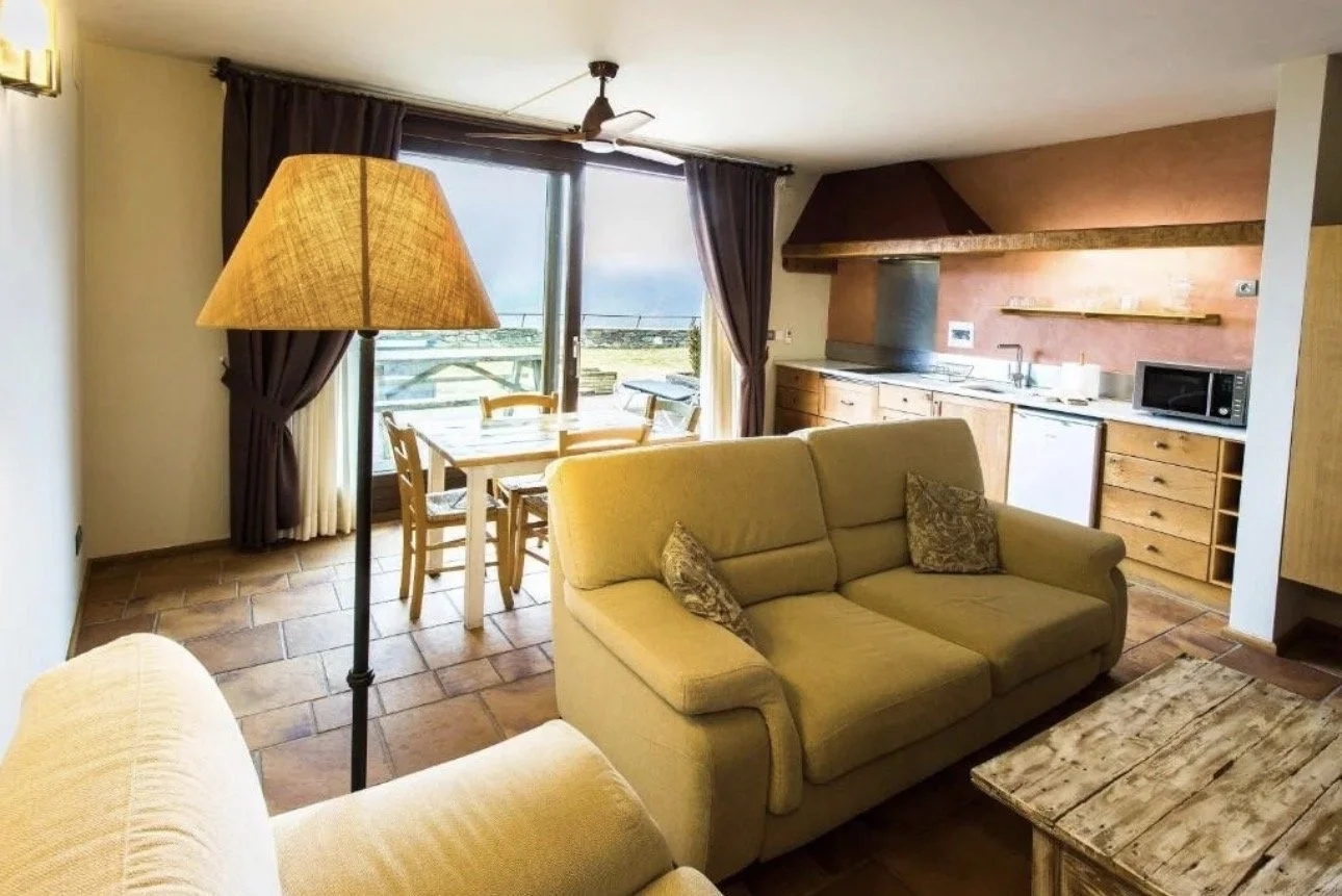 Sala de estar y cocina en un apartamento con muebles de madera y vista a un balcón con paisaje natural.