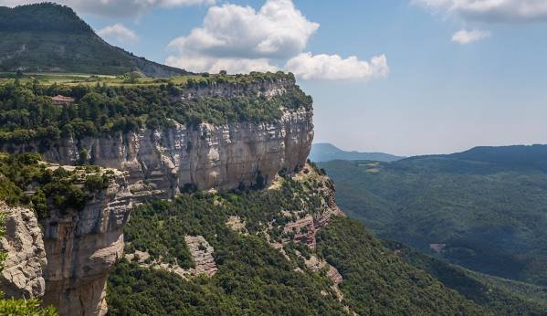 Vista de un cañón con paredes de roca y vegetación verde bajo un cielo con nubes.