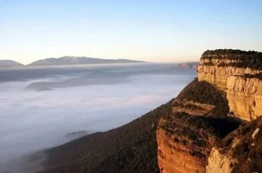 Vista de un cañón con formaciones rocosas y una capa de nubes debajo en un cielo despejado.