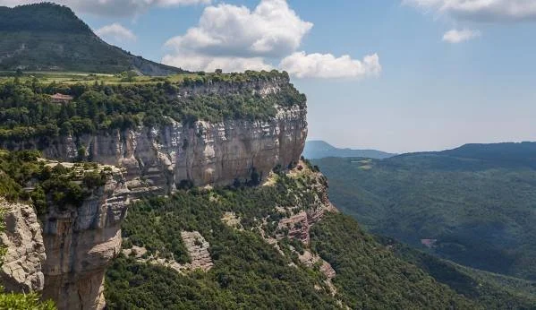 Vista de un cañón con formaciones rocosas y vegetación verde bajo un cielo con nubes.