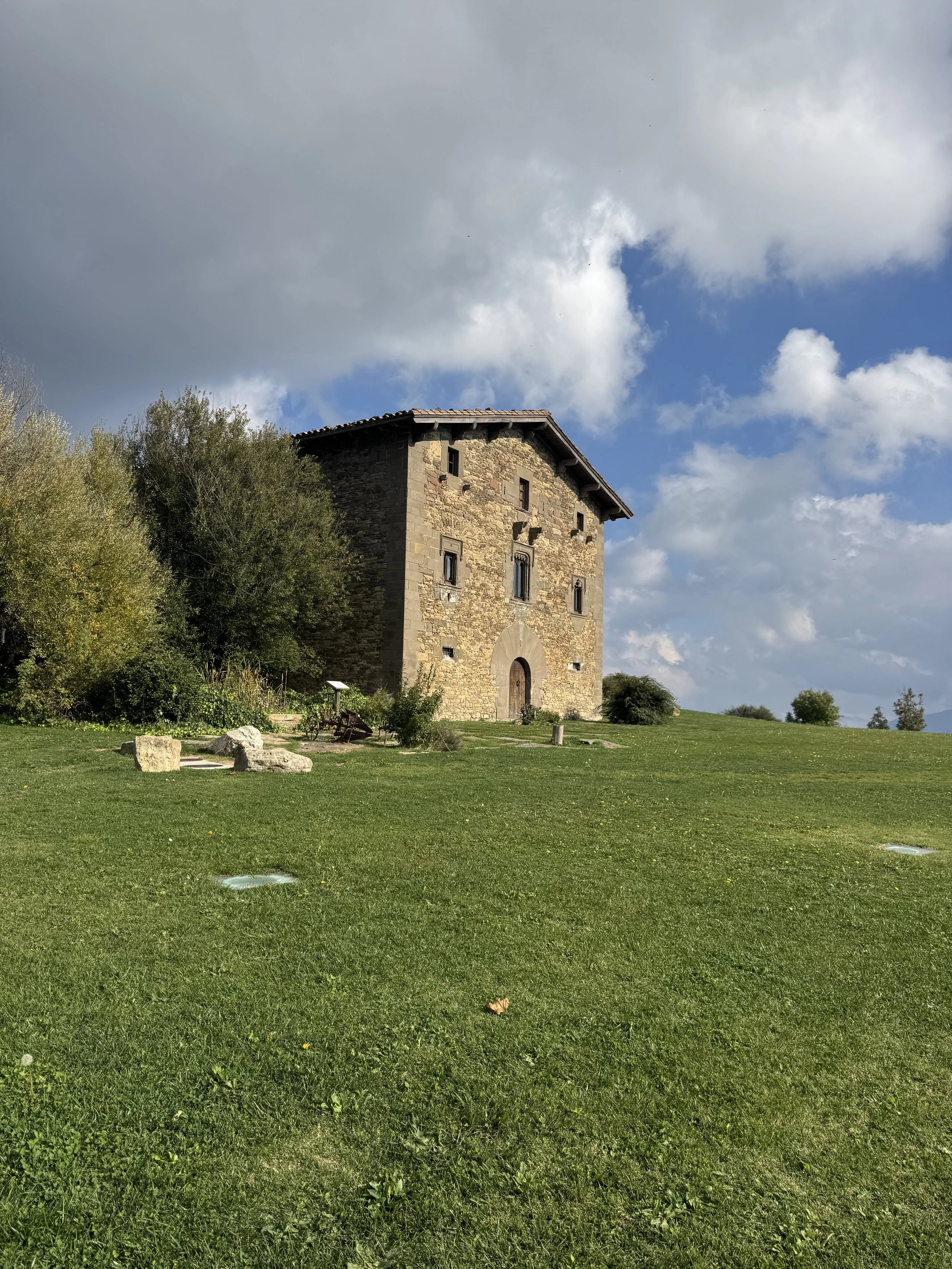 Un edificio de piedra en un campo verde con árboles y un cielo con nubes.